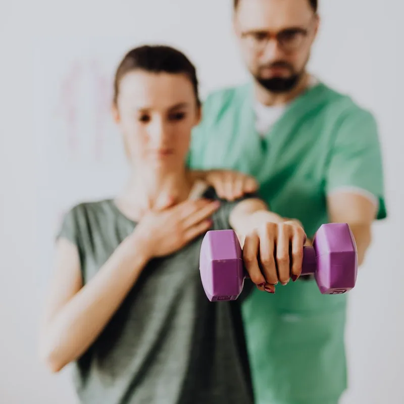 A therapist coaches a patient through a dumbbell exercise
